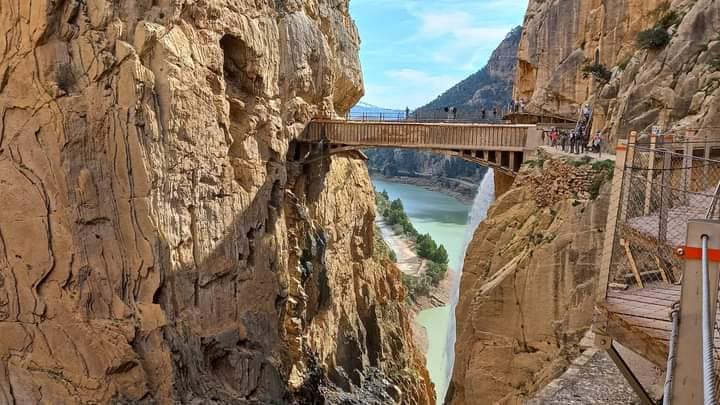 A view of a bridge between two cliffs with a blue lake in the background.